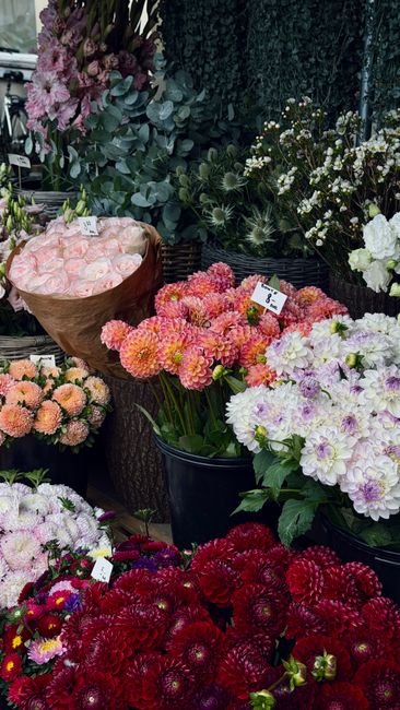 A vibrant display of fresh floral arrangements at a florist shop, featuring a variety of flowers including pink roses wrapped in brown paper, peach-colored chrysanthemums, white and pink double dahlia